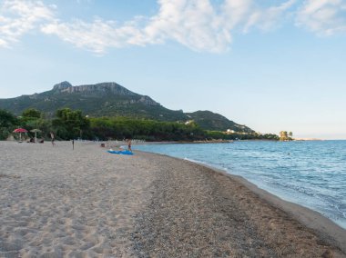 Kumsal manzarası Spiaggia di Santa Maria Navarrese denizi yeşil orman ve kireçtaşı kayası Monte Oro dağı. Altın saat ışığı, Sardunya, İtalya