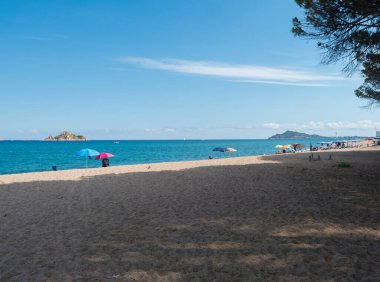 Kum sahili Spiaggia di Santa Maria Navarrese manzarası, renkli plaj şemsiyesi ve güneşlik yatakları olan deniz ve Arbatax penisula manzarası. Yaz güneşli bir gün, Sardunya, İtalya