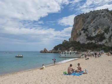 Cala Gonone, Sardinya, İtalya, 9 Eylül 'de güneşlenen insanlar ve turizm teknesi ile Cala Luna plajı. Kireç taşlı beyaz kumsal, turkuaz mavi su. Ünlü turistik tatil beldesi