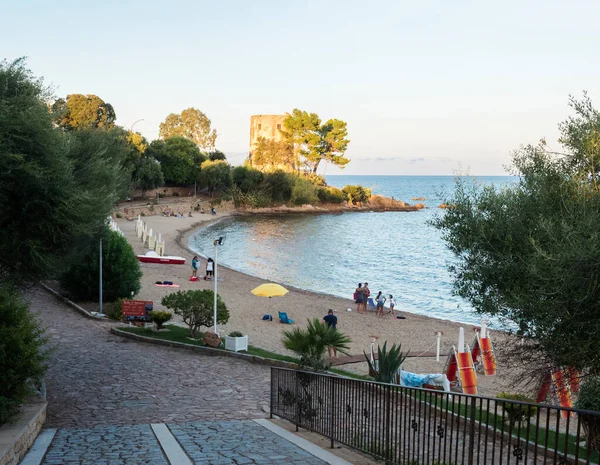 Санта Мария Наваррезе, Фелиния, Италия, 6 сентября 2020 года: вид на пляж Spiaggia di Santa Maria Navarrese с группой людей, променадом, зелеными деревьями и старой каменной башней. Золотой час — стоковое фото