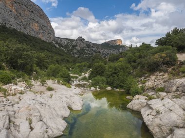 Gola Su Gorropu vadisine giden yürüyüş yolu üzerindeki kurumuş flumineddu nehri ve kireçtaşı kaya ve Akdeniz bitkisi, Nuoro, Sardinya, İtalya 'daki Supramonte Dağlarının yeşil orman manzarası.