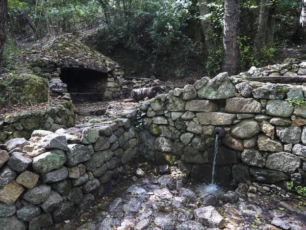 Fountain, drinkable water with resting place and fire place in forest at Supramonte Mountains on hiking trail to Gola Su Gorropu. Sardinia, Italy.