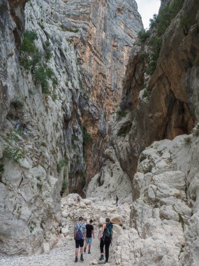 Supramonte Dağları, Nuoro, Sardinya, İtalya, 11 Eylül 2020: Kireçtaşı duvarları, yeşil çalıları ve ağaçlarıyla Gola Su Gorropu geçidinde yürüyüş yapan bir grup turist. Ünlü yürüyüş yeri.
