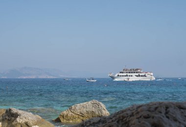 Cala Goloritze, Sardinya, İtalya, 8 Eylül 2020: Kayalık kıyılardan görülen Orosei Körfezi 'nin turkuaz mavi sularındaki turist yolcu gemisi manzarası.