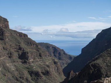 Barranco de Guayadeque vadi boyunca okyanusa bakan dik duvarlar. Gran Canaria, Kanarya Adası, İspanya. Güneşli bir gün, mavi gökyüzü, beyaz bulutlar...