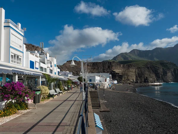 Puerto de las Nieves, Agaete, Gran Canaria, Wyspy Kanaryjskie, Hiszpania 17 grudnia 2020: Ulica wzdłuż morza i żwirowa plaża z tłem gór w Puerto de las Nieves, tradycyjna wioska rybacka — Zdjęcie stockowe