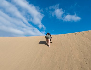 İspanya 'nın Kanarya Adaları' ndaki Gran Kanarya Adaları 'ndaki Maspalom' un Doğal Rezervi 'ndeki altın kum tepeciğindeki sırt tırmanışından genç bir kadın. Mavi gökyüzü arkaplanı