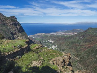Gran Canaria 'nın kuzeybatısındaki kayalık ve kayalık Atlantik kıyıları Agaete şehri, yılan yolu ve yeşil tepeler manzaralı. Kanarya Adaları, İspanya.