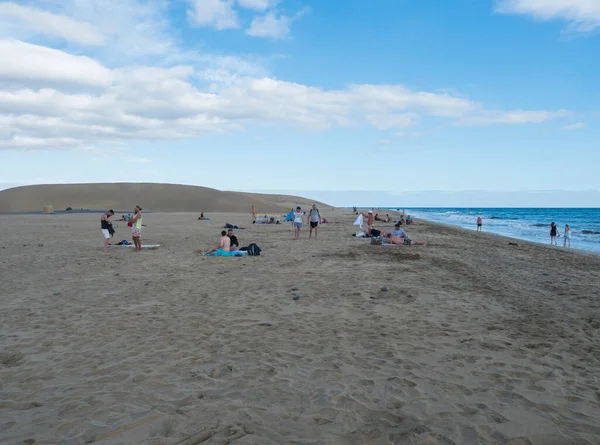 Maspalomas, Gran Canaria, Kanári-szigetek, Spanyolország 2020. december 18.: Maspalomasi Dunes természeti rezervátumának strandján napozó turisták csoportja, arany homokdűnék, kék ég. — Stock Fotó