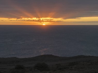Atlantik Okyanusu 'na inen kızıl turuncu güneşli güzel bir gün batımı. Koyu mavi bulutlar ve deniz.