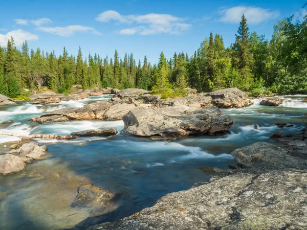 Piękny krajobraz z długą ekspozycją strumienia wody i kaskady rzeki Kamajokk, głazy i świerk lasu drzewa w miejscowości Kvikkjokk w szwedzkiej Laponii. Letni słoneczny dzień, błękitne niebo, białe chmury — Zdjęcie stockowe