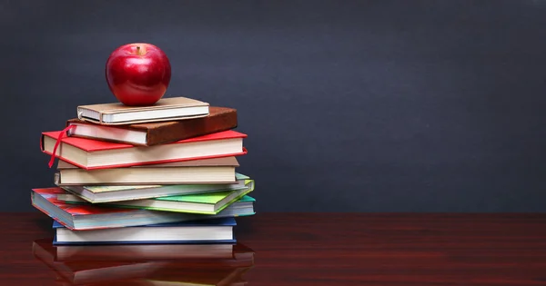 Pile of books and red apple on the desk over the blackboard — Stock Photo, Image