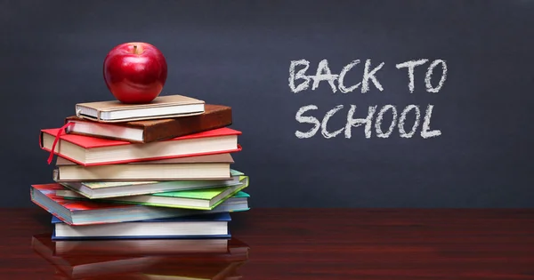 Pile of books and red apple on the desk over the blackboard — Stock Photo, Image