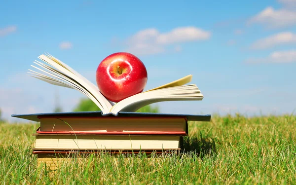 De vuelta a la escuela. Libro abierto y manzana sobre hierba verde — Foto de Stock