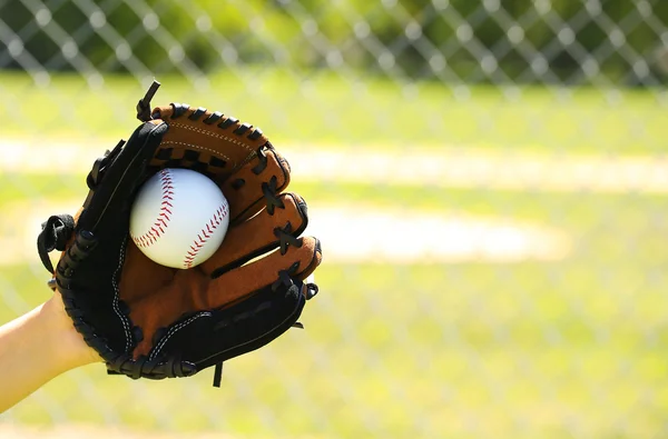 Mão do jogador de beisebol com luva e bola sobre campo e rede — Fotografia de Stock
