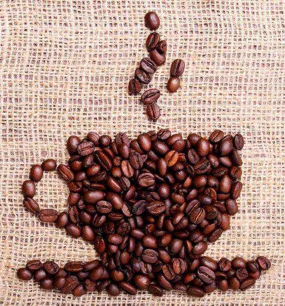 Graines de café sur toile de jute, placées en forme de tasse — Photo