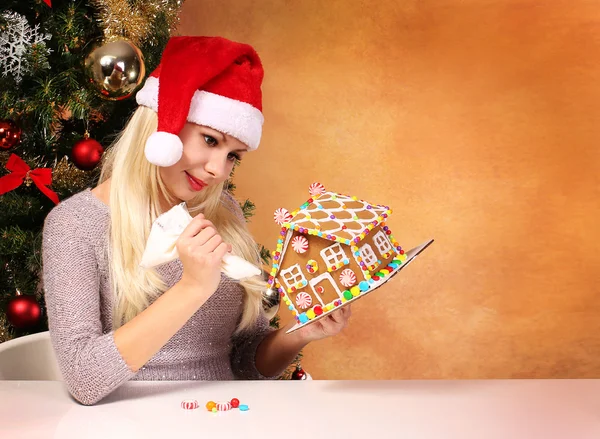 Girl making gingerbread house. Young woman with Santa Hat — Stock Photo, Image