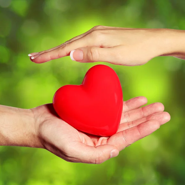 Corazón de San Valentín en manos femeninas y masculinas, sobre la naturaleza Green Sunn — Foto de Stock