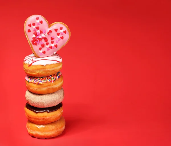 Sweet donuts with heart shaped donut on the top over red backgro — Stock Photo, Image