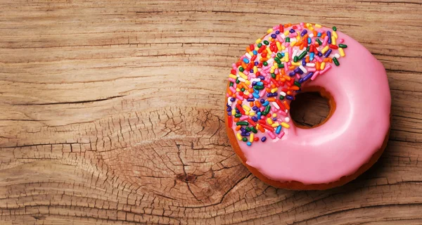 Donut with sprinkles on wooden background — Stock Photo, Image