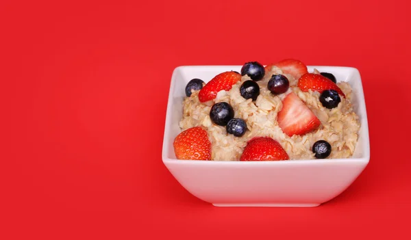 Haferflocken mit Beeren auf rotem Hintergrund — Stockfoto