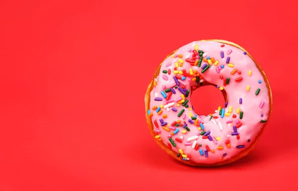 Donut with sprinkles over red background — Stock Photo, Image