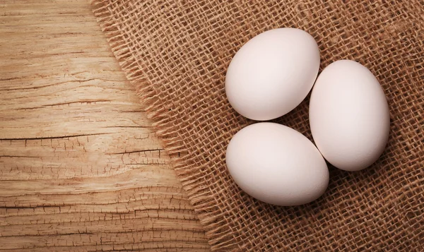 Huevos blancos en arpillera sobre fondo de madera —  Fotos de Stock