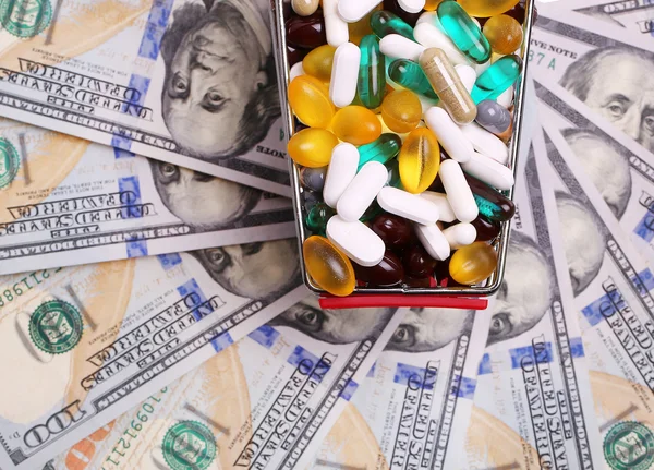 Shopping cart full with pills and capsules over dollar bills — Stock Photo, Image