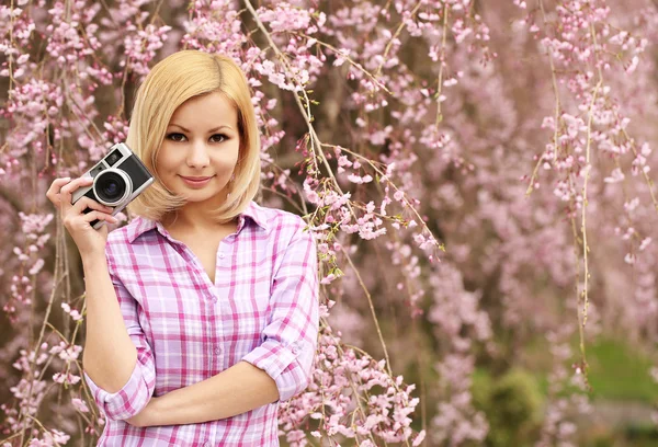Fotógrafo. Chica rubia con cámara retro sobre flor de cerezo . — Foto de Stock
