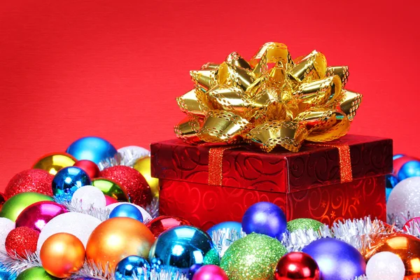 De gift van Kerstmis met kleurrijke ballen over rode backgro en gouden boog — Stockfoto
