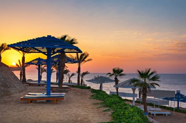 Palmiye ağaçları ve güneşli bir sahil ya da lüks bir otelde güneşli bir yatak. Mısır tatil köyünde gün doğumu