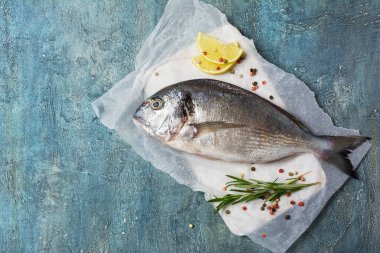 Taze balık dorado 'nun üst görüntüsü ya da limon ve baharat içeren yaldızlı çipura ahşap kesim tahtasında biberiye ve mavi beton arka plan.
