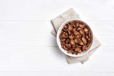 Kahvaltıda çikolatalı gevrek ile birlikte beyaz ahşap arka planda fotokopi alanı olan kasenin üst görüntüsü.