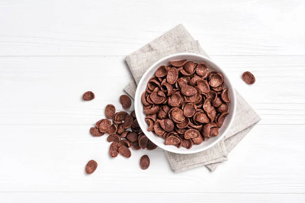 Beyaz ahşap arka planda kahvaltıda çikolatalı gevrek ve şekerli kase manzarası.