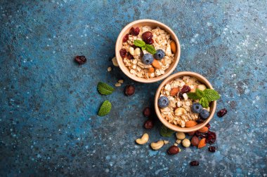 Taze yaban mersinli, bademli, fındıklı, fındıklı yeşil nane yapraklı yulaf ezmesi sağlıklı kahvaltı için mavi beton arka planda fotokopi alanı olan yeşil nane yapraklı.