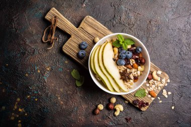 Taze armut, yabanmersini, badem, fındık ve fındık ezmeli yulaf ezmesi, kahverengi beton zemin üzerinde sağlıklı kahvaltı için yeşil nane yaprağı.