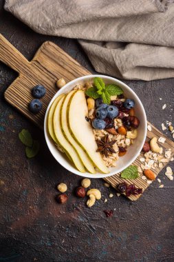 Taze armut, yabanmersini, badem, fındık ve fındık ezmeli yulaf ezmesi, kahverengi beton zemin üzerinde sağlıklı kahvaltı için yeşil nane yaprağı.