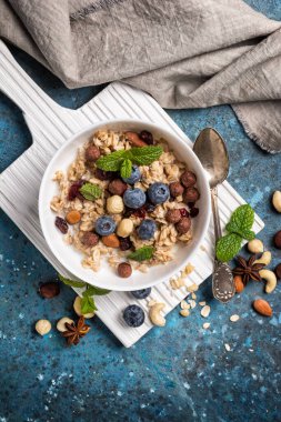 Sütlü yulaf ezmesi, taze yaban mersini, badem, fındık ve fındık, yeşil nane yaprağı sağlıklı kahvaltı için mavi beton arka planda