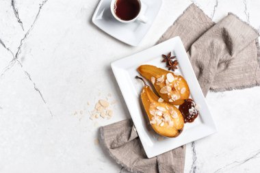 Meyve tatlısı, fırında armut, karamel sosu, peynir kremi ve badem gevreği beyaz mermer arka planda fotokopi alanı.