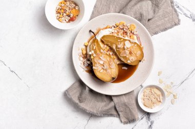 Meyve tatlısı, fırında armut, karamel sosu, peynir kremi ve badem gevreği beyaz mermer arka planda fotokopi alanı.