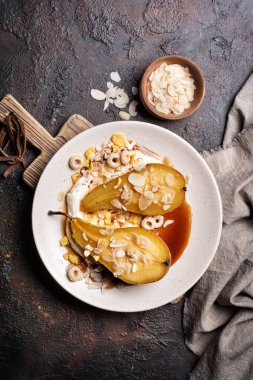 Meyve tatlısı, fırında armut, karamel sosu, peynir kremi ve koyu beton arka planda badem gevreği.
