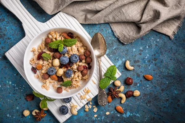 Top view of oatmeal with milk, fresh blueberry, almonds, hazelnuts and cashews nuts, green mint leaves for healthy breakfast on blue concrete background