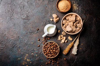 Kahverengi kamış şekerli, yumrulu, granüllü, kristal şeker çubuklu, kahve çekirdekli, lezzetli içecekler ya da koyu beton arka planda fotokopi alanı olan içecekler için süt içeren kaselerin üst görüntüsü