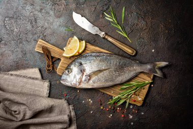 Taze balık dorado ya da biber, biberiye, ahşap kesim tahtasında limon ve kahverengi beton arka planda baharatlı yaldızlı karagöz.