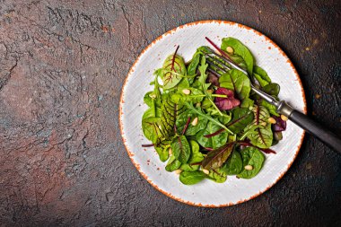 Taze yeşil yapraklar ve koyu grunge beton arka planda çam fıstığı karışımı vejetaryen salatasının en üst görüntüsü.