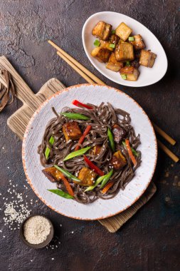 Lezzetli Japon sobalı şehriye, kırmızı dolma biber, yeşil soğan, kızarmış tofu peyniri ve kahverengi beton arka planda susamlı susam.