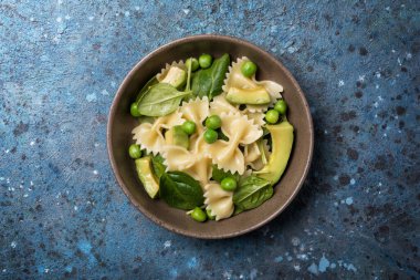 Yeşil bezelye, avokado ve mavi beton arka planda ıspanak yapraklı lezzetli vejetaryen farfalle makarna manzarası.