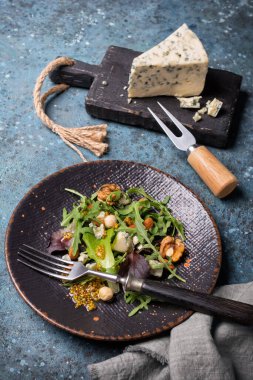 Sağlıklı ve lezzetli vejetaryen yemekleri. Taze yeşil yapraklı salata, mavi peynir, fındık ve hardal sosu mavi beton arka planda.