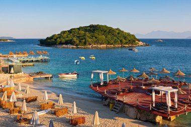Arnavutluk kıyılarında kumsal, ada, şemsiye ve mavi İyon deniziyle güzel bir sabah manzarası