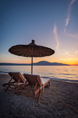 Arnavutluk 'un İyon Denizi kıyısında iki plaj sandalyesi ve şemsiyeli güzel gün batımı deniz manzarası